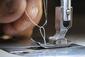 Hand of the seamstress pulling a brown thread into the needle hole of the industrial sewing machine close-up.