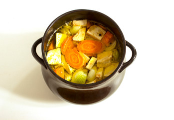 Clear Chicken broth with pieces of vegetables and spices in saucepan. Cooking chicken soup with vegetables in large clay black pot. 