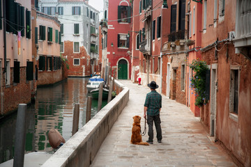Fototapeta na wymiar A man with a dog on a waterfront in Venice. Traveling with a pet. Nova Scotia Duck Tolling Retriever with the city