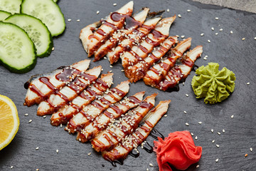 Smoked eel sliced fillet with fresh cucumber, pickled ginger and wasabi on slate plate