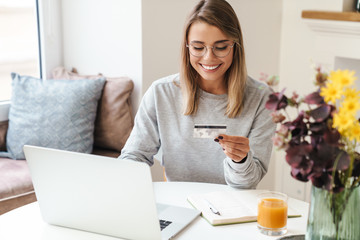 Photo of smiling woman using laptop while holding credit card - obrazy, fototapety, plakaty