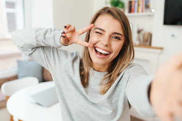 Photo of woman gesturing peace sign and winking while taking selfie