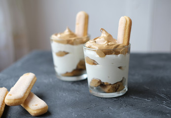 Iced frothy Dalgona Coffee tiramisu in a glass, a trendy fluffy creamy whipped coffee on the top of tiramisu dessert. Korean drink latte espresso with coffee foam.