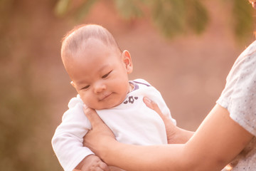 Cute baby in her mother arms outdoors portrait. asian having fun with little son, holding up male infant with arms mom standing beside at outdoor public park,  Mother's Day concept