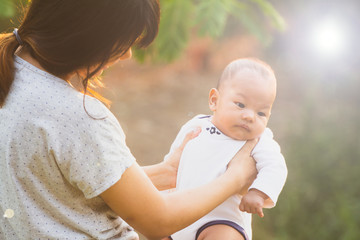 Cute baby in her mother arms outdoors portrait. asian having fun with little son, holding up male infant with arms mom standing beside at outdoor public park,  Mother's Day concept