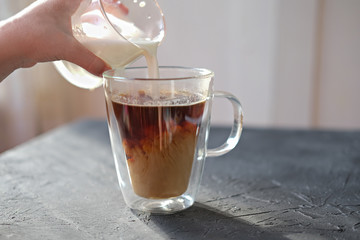 little girl's hand holding glass of milk and pouring milk into a cup of coffee. coffee with milk for breakfast. coffee cup under morning sunlight 
