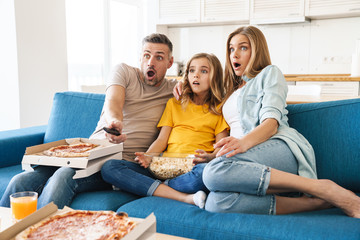 Photo of scared family eating popcorn and pizza while watching tv