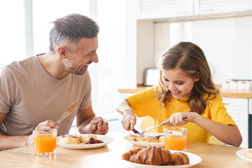 Photo of father and daughter laughing while having breakfast in kitchen
