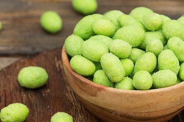 Fried peanuts in wasabi in a wooden bowl on a brown wooden table. Rustic style. Peanuts in wasabi close up