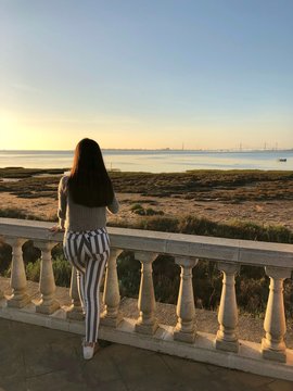 chica/mujer guapa apoyada en una valla con increible paisaje de playa de san fernando, cadiz antes de atardecer con un bonito cielo despejado