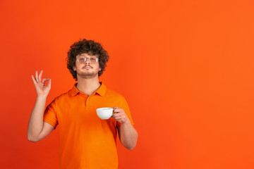 Nice coffee, delighted. Caucasian young man's monochrome portrait on orange studio background....