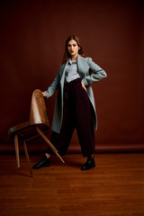 Independent young woman posing in the photostudio. Gorgeous young female in classic suit and grey coat.