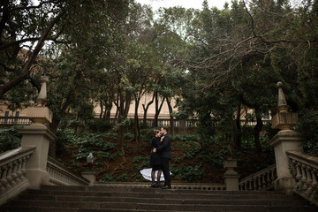 Fototapeta premium Young beautiful loving Hispanic couple walks under an umbrella during the rain in Plaza Spain. Couple posing against the backdrop of the National Museum of Art of Catalonia.
