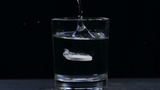 The tablet falls into a glass of water. effervescent tablet aspirin. close-up on a black background.Slow motion