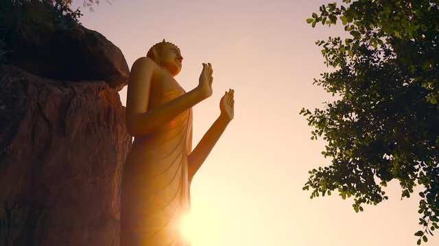 Golden statue of the standing Buddha at sunset on the monkey mountain in Hua hin. Standing Buddha in the sun rays of the sunset. Khao Takiab - Monkey or Chopstick mountain.