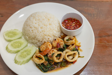 Pad Kra Pao Seafood(Thai food) - fried shrimps and squids with holy basil beside cooked rice and Chilli Fish Sauce - Stock Photo
