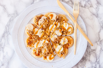 Belgium heart shaped waffles with bananas, maple syrup, salted caramel and nuts. Top view.