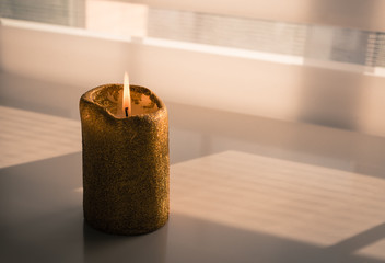 Burning candle on a wooden table next to a window through which a faint evening light enters