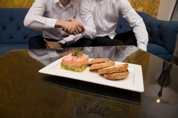 salmon avocado and rucola appetizer, .white bread cracker on a white plate.