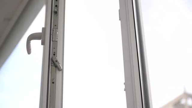 A man opens and closes a white plastic window by the handle.