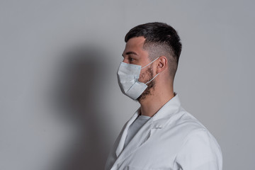 portrait of a brunette man doctor in a white coat with a mask on his face on a white background