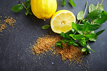 Organic lemon, mint leaves and cane sugar on dark stone background. Ingredients for homemade...