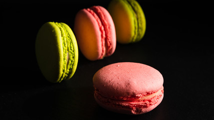 sweets advertising concept, french dessert - pink and pistachio macaroons on a black background, close-up