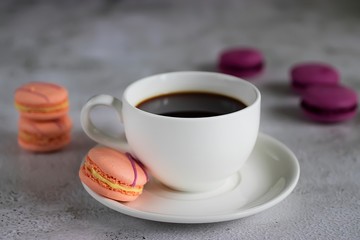 White cup with black coffee and bright macaroon cakes on a concrete background.