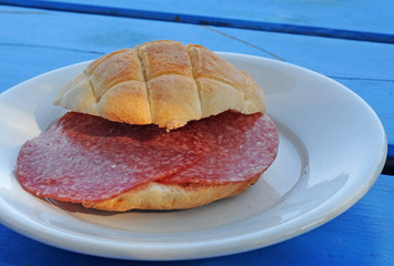 Typical Italian bread roll with salami on white plate on blue painted wooden table