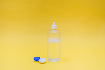Clear solution for lenses and a white container on a yellow background. Lens care. Eye problem. Farsightedness and myopia.