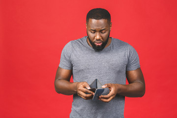 Poverty crisis concept. Upset african american young bearded man in casual holding empty wallet over red background.