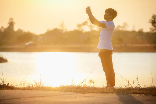 man holding a cellphone taking pictures outside during sunrise or sunset.