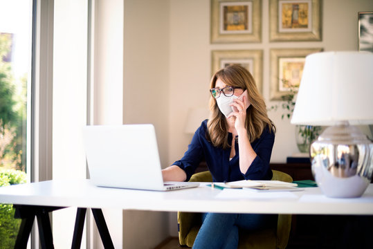 Confident Mature Woman Making A Call And Using Laptop While Working At Home During Coronavirus Pandemic