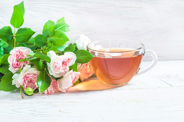 Tea time concept. Glass cup of tea and bunch of rose flowers on rustic white paint wooden background
