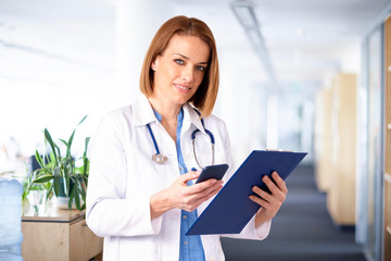 Femal doctor text messaging while standing in medical clinic
