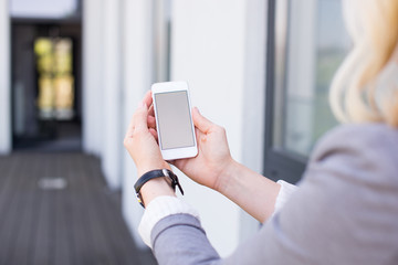 Mockup blonde woman watching her smartphone with empty screen in a modern building. Real Estate Agent with mockup smartphone. Young woman with phone in green background