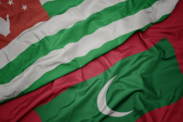 Obraz premium waving colorful flag of maldives and national flag of abkhazia.