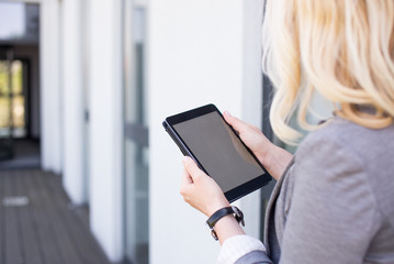 Mockup blonde woman watching her tablet with empty screen in a modern building. Real Estate Agent with mockup tablet. Young woman with tablet in green background