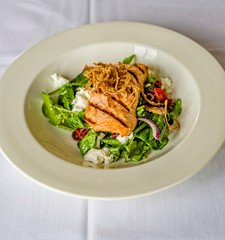Stacked grilled salmon with onion rings salad, vegetable, and sauce on white plate