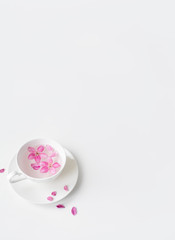Spring background for the inscription, pink flowers, sakura cherry blossoms, cup with water and flower petals, fashion trend of the year, top view, creative banner, copy space flat lay