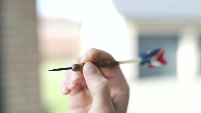 A girls hand about to throw a red, white and blue darts arrow dart. She is holding the point just in focus before the throw. Extreme close up with nice depth of field.