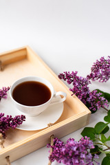  porcelain cup with coffee, cocoa, spring breakfast on a wooden tray. Branches and flowers of lilac, violet color, on a white background. Minimalistic design