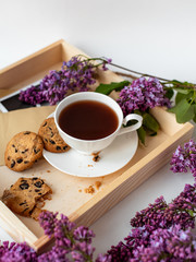 Cup with coffee, cocoa, chocolate chip cookies, spring breakfast on a wooden tray. Lilac branches, a bouquet of purple color, on a white background. Minimalistic design, top view, creative flat lay