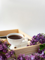 Obraz na płótnie Canvas Cup with coffee, cocoa, spring breakfast on a wooden tray. Lilac branches, a bouquet of purple color, on a white background. Minimalistic design, top view, creative frame, copy space