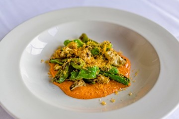 Grilled cauliflower, blistered, Spanish-style, padron peppers, grilled onions, and roasted red pepper sauce in a white bowl.