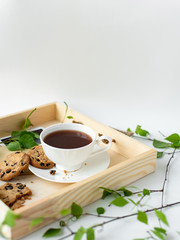 Cup with coffee, cocoa, chocolate chip cookies, spring breakfast on a wooden tray. Branches with leaves, greenery, on a white background. Minimalistic design, creative banner, with copy space