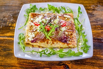 Greek salad crepe sandwich with arugula, tomatoes, cucumber, and feta cheese on white decorated plate.