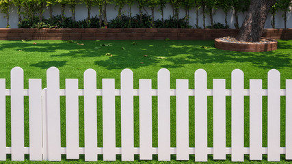 Front view of white wooden fence in front of artificial turf with green plant growing on...