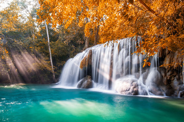 Fototapeta na wymiar Waterfall and blue emerald water in autumn forest with sun flare and sunlight in morning. Erawan Waterfall step 2nd. Beautiful nature rock waterfall steps in rainforest at Kanchanaburi, Thailand