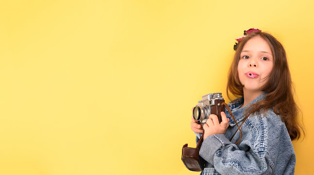 Little girl with a retro camera on a yellow background. The child shows happy emotions and poses. Tourism concept. Copy space